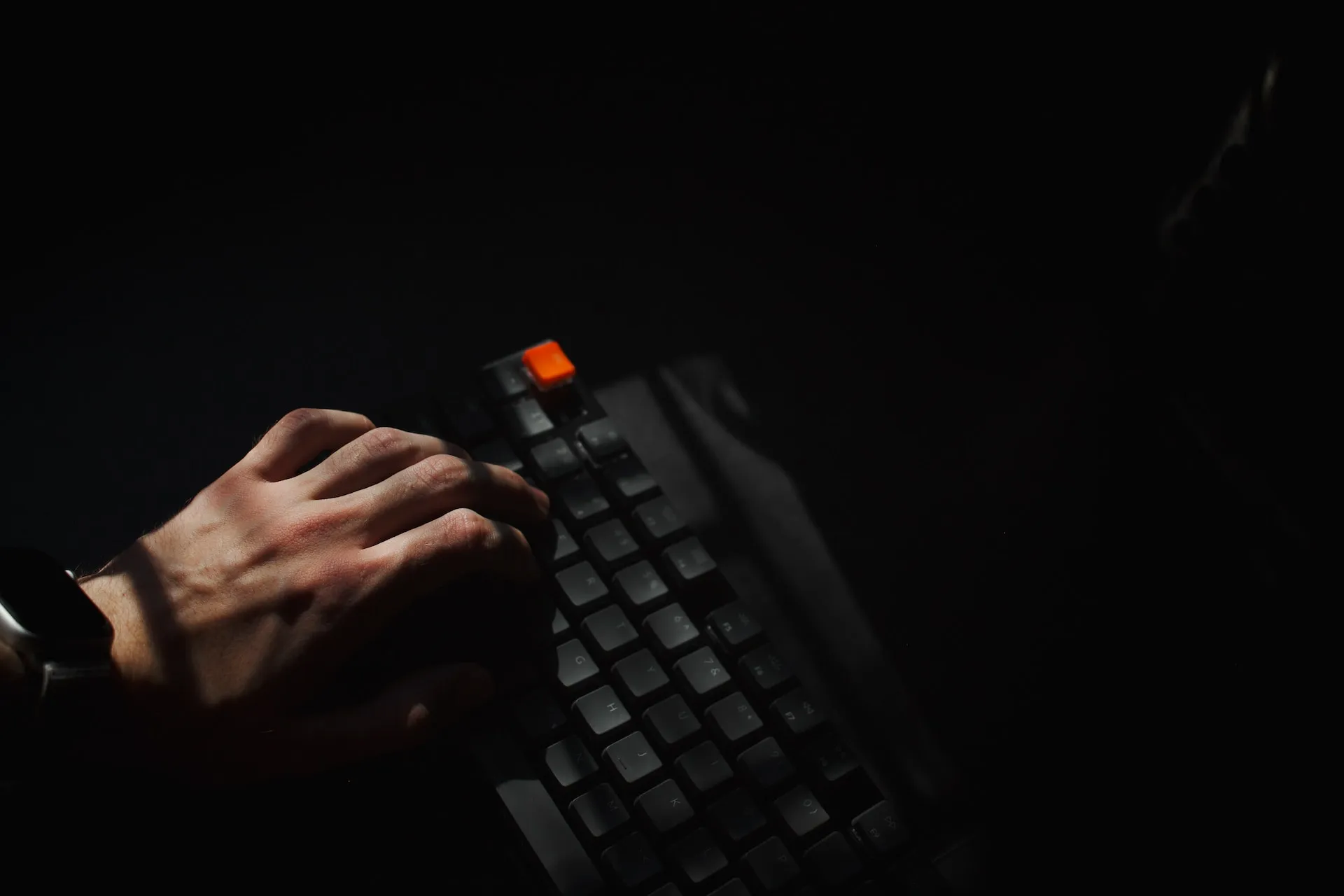 A hand typing on a dark keyboard