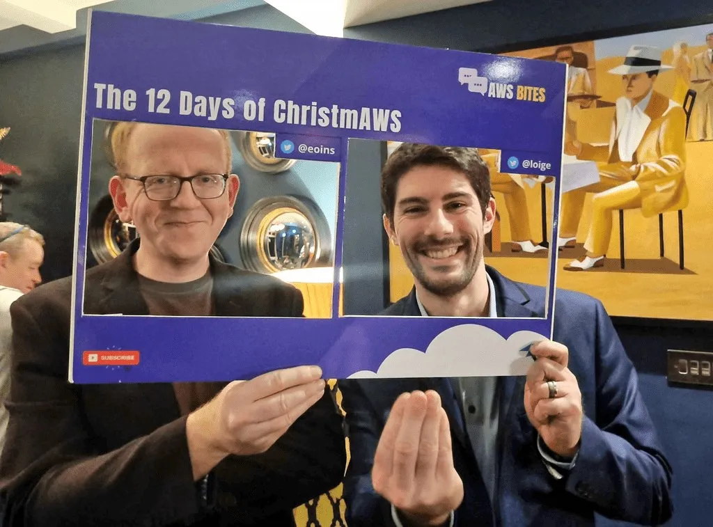 Eoin and Luciano from AWS Bites standing behind a fake cutout representing our usual AWS Bites background frame. Luciano is doing the usual Italian pinch-hand gesture