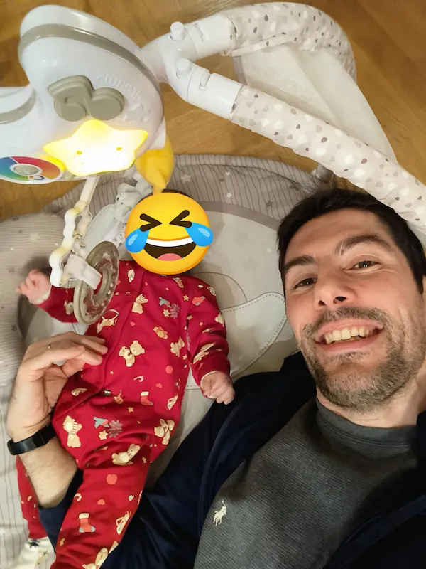 A photo of Luciano Mammino smiling with his son. The face of the baby is covered with a heart eyes emoji