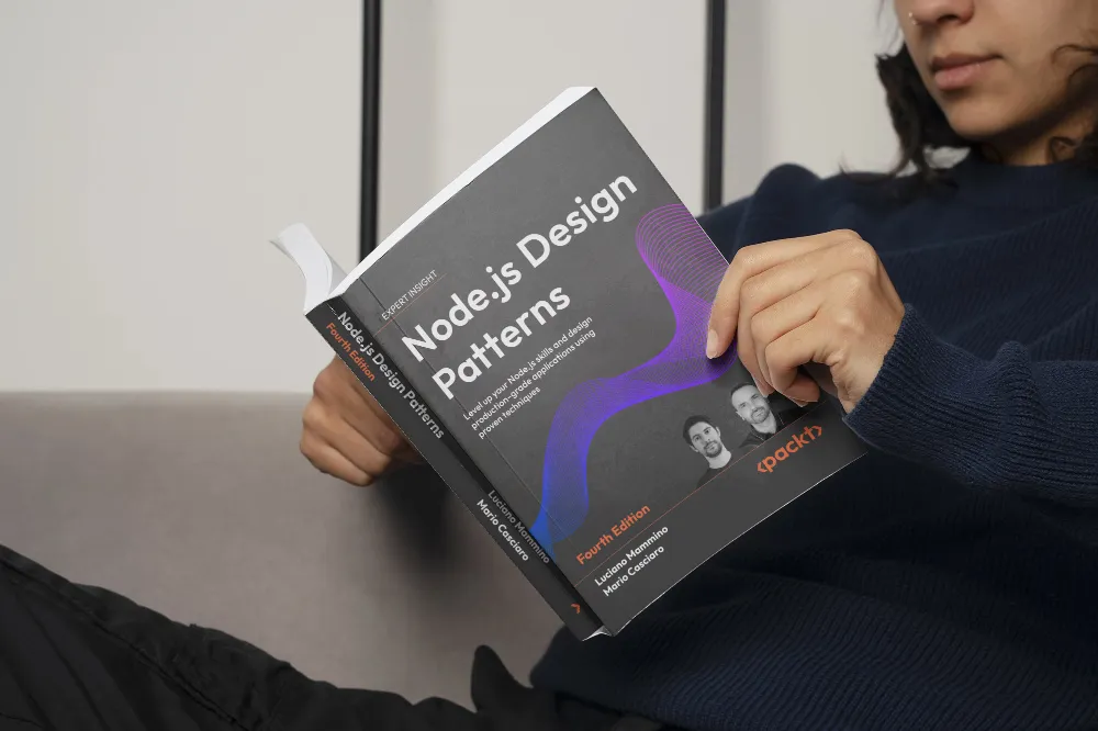 A person sitting on a couch, holding and reading the book ‘Node.js Design Patterns (Fourth Edition)’